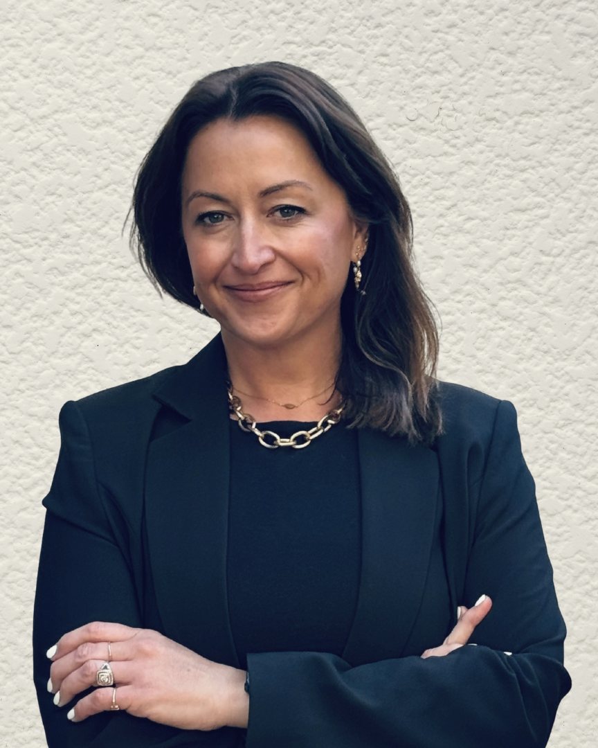 Cathy Cousins in a black blazer, arms crossed, against a white wall